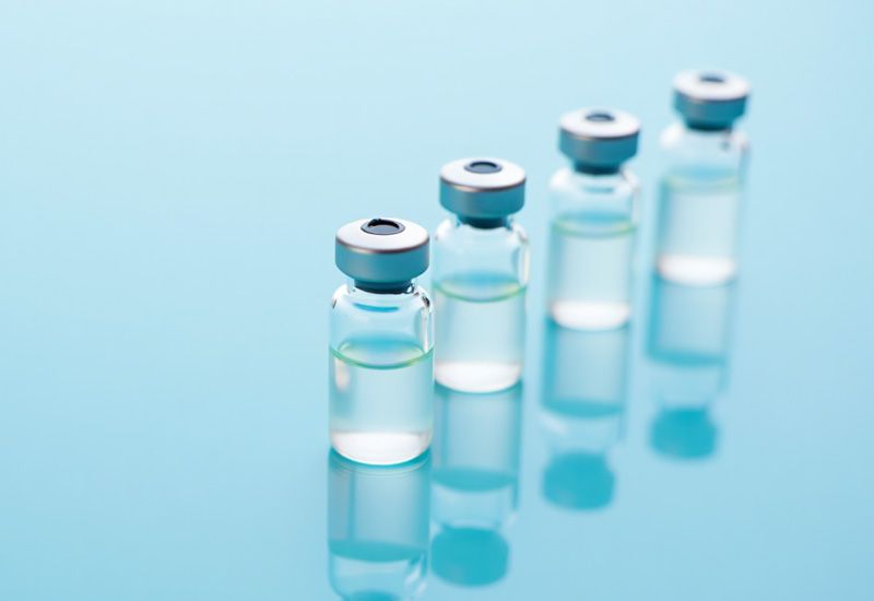 Четыре ампулы с прозрачной жидкостью стоят на голубом столе под ярким освещением